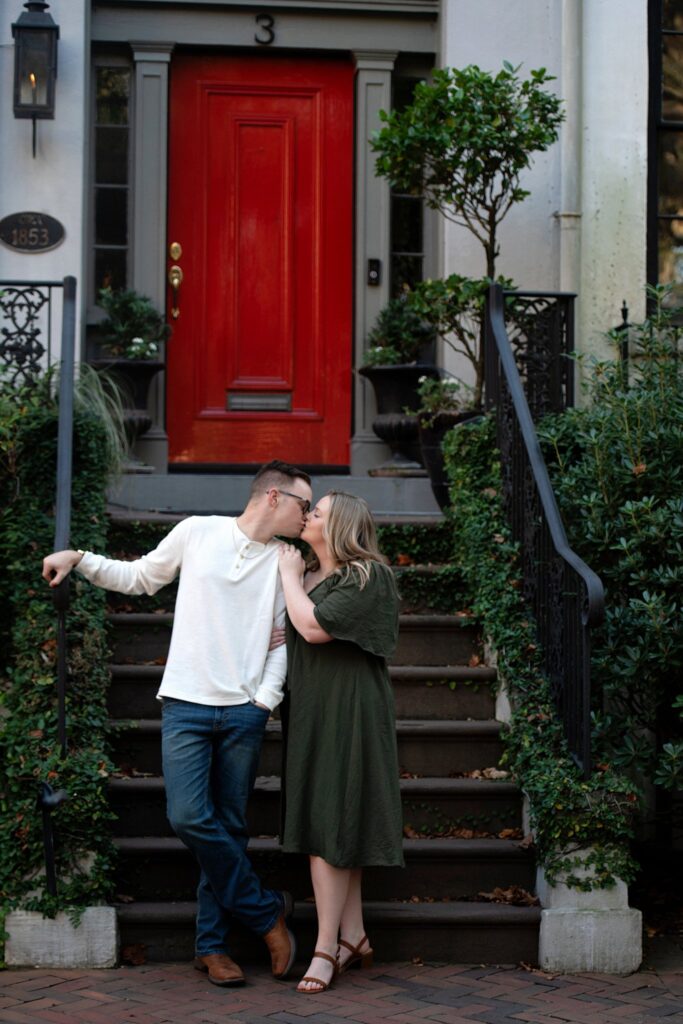 couple kissing in front of stairs and a red door