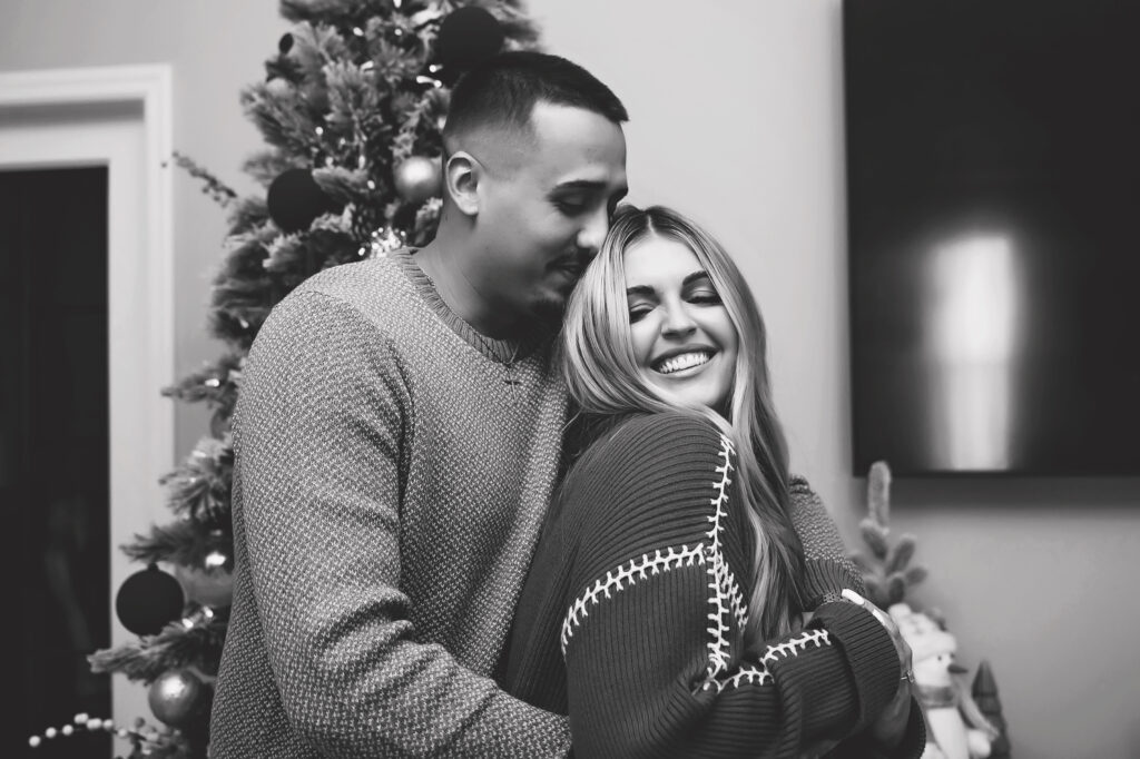 couple snuggling in front of christmas tree for engagement session