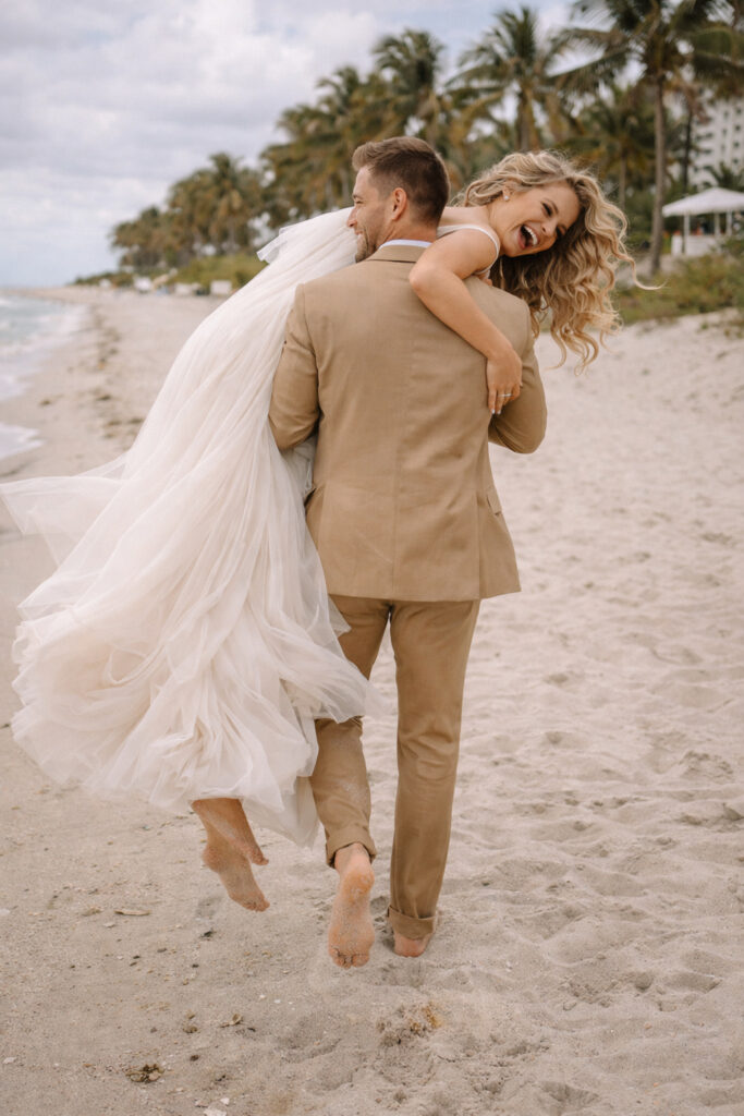 a groom carrying his bride on the beach on their wedding day in miami fl